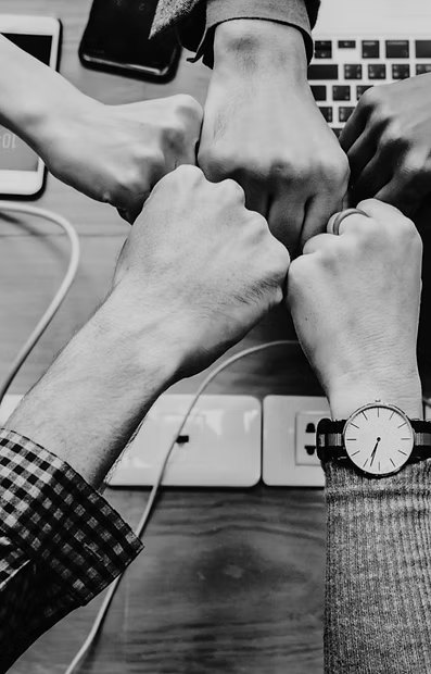 Five hands joined in a fist bump over a desk with a laptop.